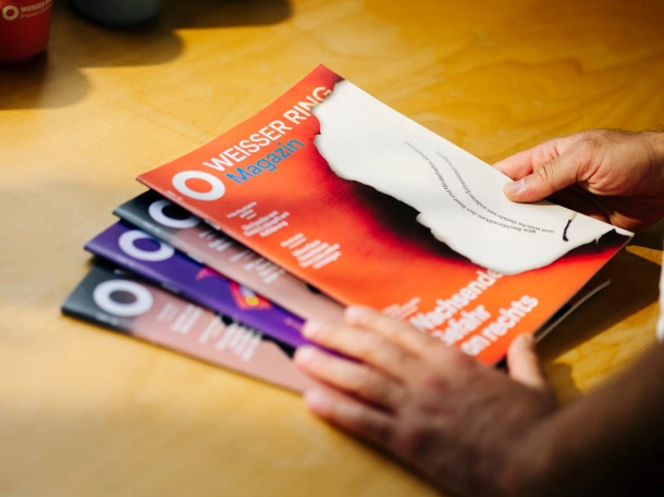 Eine Hand hält vier Ausgaben vom WEISSER RING Magazin