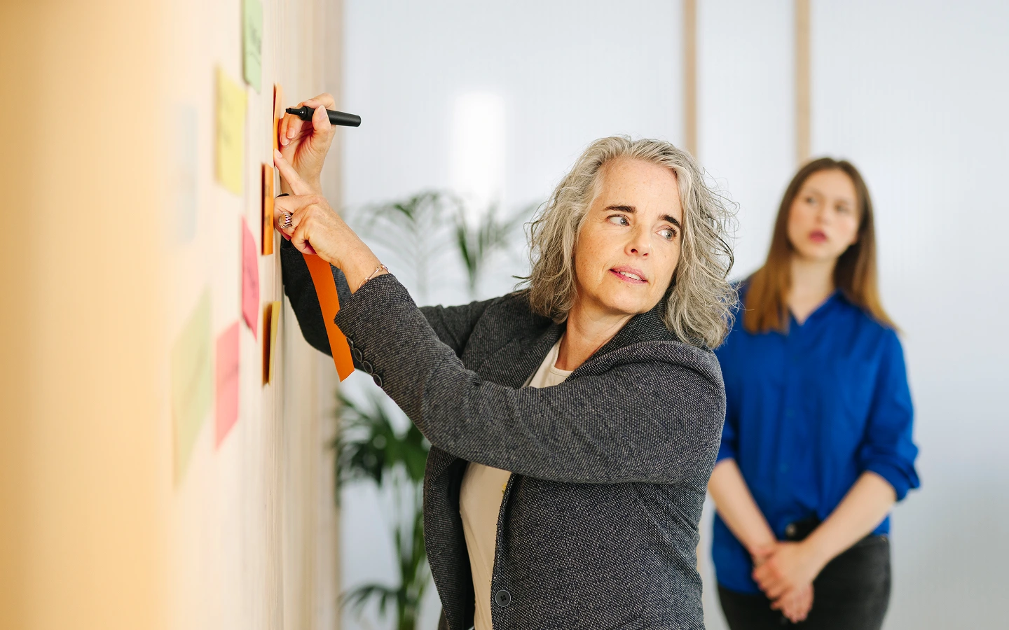 Eine Frau schreibt an einer Wand auf bunte Post-its